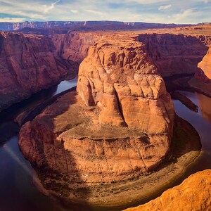 May include: An aerial view of a horseshoe-shaped canyon with a river winding through it. The canyon walls are a reddish-brown color and the river is a deep blue. The canyon is located in a desert environment.