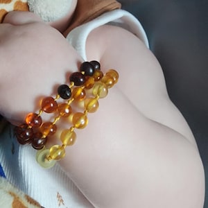 May include: A set of three beaded bracelets featuring polished amber stones in varying shades of dark brown, cognac, and honey yellow, strung on a thin yellow cord. The beads are smooth, rounded, and translucent, showcasing natural color variations.