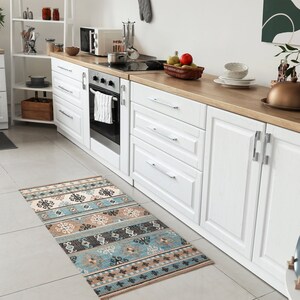 May include: A white kitchen with white cabinets and a patterned rug. The cabinets have silver handles and the rug has a blue, brown, and white geometric pattern.