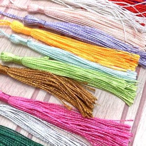 May include: A collection of colourful tassels with various lengths and textures. The tassels are made of different materials, including silk, cotton, and wool. The tassels are arranged in a row on a wooden surface.