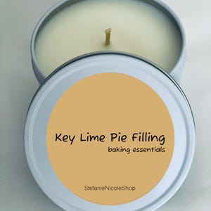 May include: A round, light blue tin candle with a cream-colored wax and a single wick. The lid features a light orange circle with the text "Key Lime Pie Filling" and "baking essentials". The shop name "StefanieNicoleShop" is also printed on the lid.