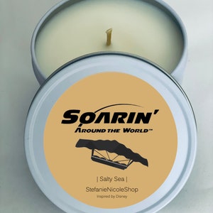 May include: A white candle tin with a beige label featuring the text "SOARIN' AROUND THE WORLD™" and a black silhouette of a hang glider. The label also includes the text "| Salty Sea | StefanieNicoleShop Inspired by Disney".