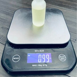 Pu&ograve; includere: Una bottiglia di vetro trasparente con una finitura opaca che contiene un liquido giallo chiaro &egrave; posizionata su una bilancia digitale. La bilancia indica 0,99 oz. La bilancia &egrave; nera con una piattaforma argentata e un display digitale. La bilancia ha pulsanti per la modalit&agrave;, accensione/spegnimento e zero.