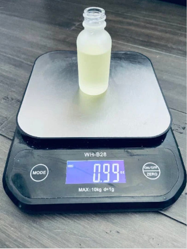 Pu&ograve; includere: Una bottiglia di vetro trasparente con una finitura opaca che contiene un liquido giallo chiaro &egrave; posizionata su una bilancia digitale. La bilancia indica 0,99 oz. La bilancia &egrave; nera con una piattaforma argentata e un display digitale. La bilancia ha pulsanti per la modalit&agrave;, accensione/spegnimento e zero.