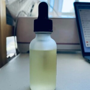 Pu&ograve; includere: Una bottiglia di vetro trasparente con una finitura opaca e un contagocce nero in cima. La bottiglia &egrave; piena di un liquido giallo chiaro.