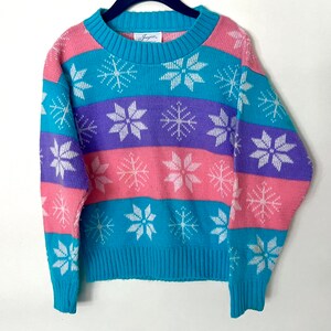 May include: A turquoise, pink, and purple striped sweater with a white snowflake pattern. The sweater has a crew neck and long sleeves.
