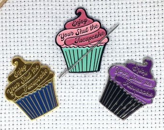 May include: Three cupcake enamel pins with the text "Enjoy Your Shut the F*ck Up Cupcake". The pins are gold, blue and black with pink, purple and green frosting.