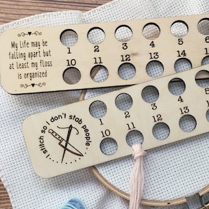 May include: Wooden floss organizer with 16 slots for holding embroidery floss. The organizer has the text "My life may be falling apart but at least my floss is organized" and "stitch so I don't stab people".