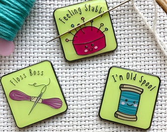Può includere: Tre spille in smalto con sfondo verde chiaro e contorni neri. La prima spilla presenta un cuscinetto per spilli rosso con un ago e il testo "Feeling Stabby". La seconda spilla presenta un rocchetto di filo con un ago e il testo "Floss Boss". La terza spilla presenta un rocchetto di filo con il testo "I'm Old Spool".