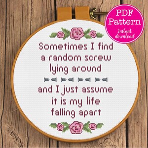 May include: A white embroidery hoop with a cross-stitch pattern that reads "Sometimes I find a random screw lying around and I just assume it is my life falling apart". The hoop is decorated with pink flowers and green leaves.