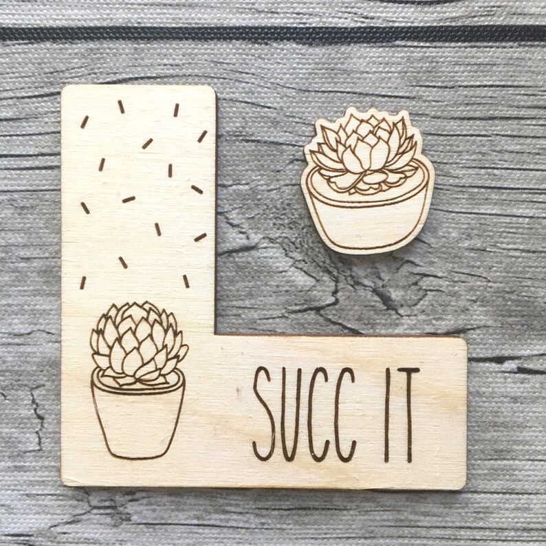 K&ouml;nnte beinhalten: Ein Holzschild mit einem Sukkulenten-Design und dem Text "SUCC IT" in einer handschriftlichen Schrift.