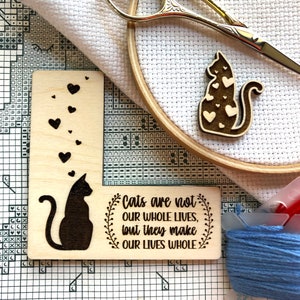 May include: A wooden sign with a black silhouette of a cat and hearts. The sign reads "Cats are not our whole lives, but they make our lives whole."