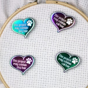 May include: Four iridescent heart-shaped pins with white paw prints and text that reads "This project may contain dog hair" and "This project may contain cat hair".
