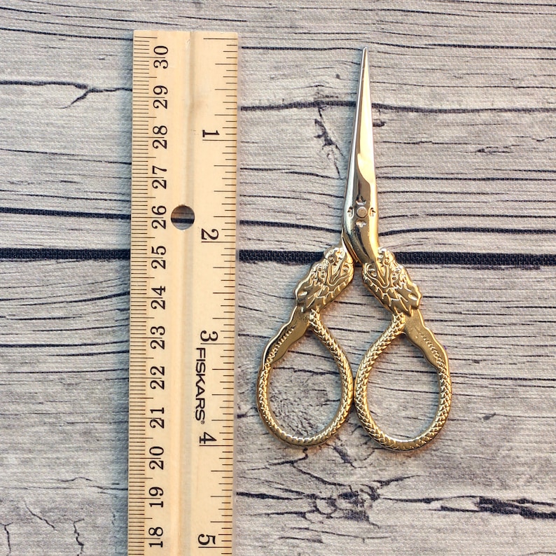May include: Gold-toned scissors with a snake design. The scissors are 3 inches long and are measured against a ruler.