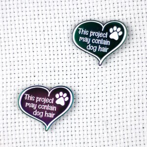 May include: Two iridescent heart-shaped pins with a white paw print and the text "This project may contain dog hair".
