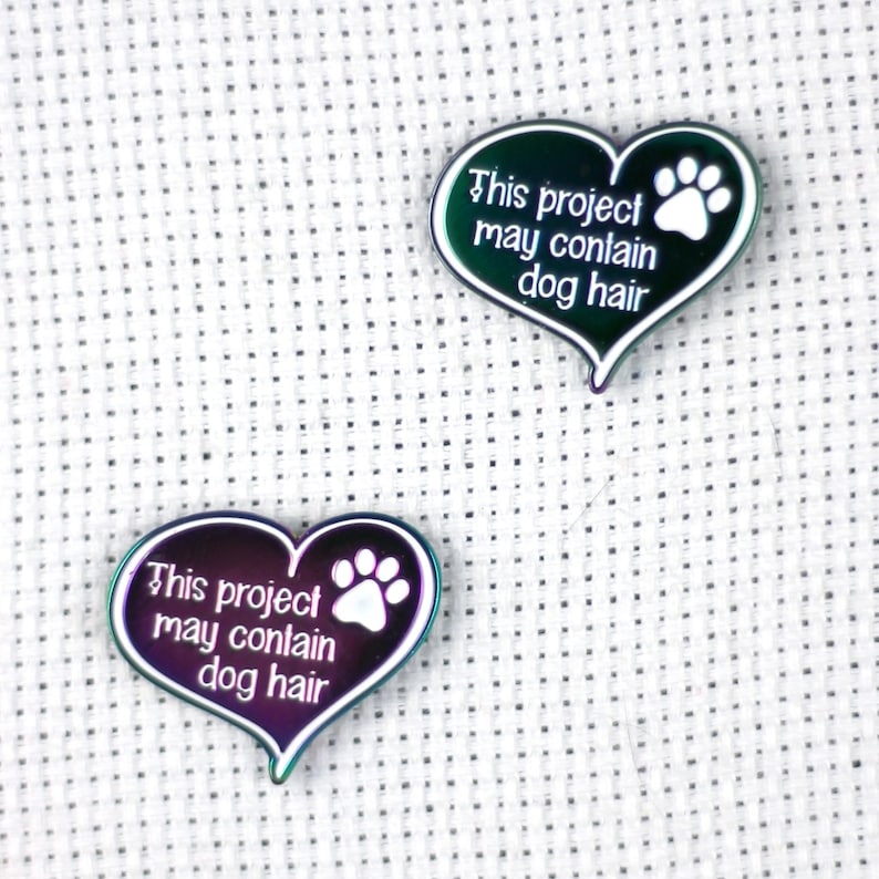 May include: Two iridescent heart-shaped pins with a white paw print and the text "This project may contain dog hair".