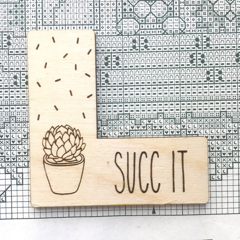 K&ouml;nnte beinhalten: Ein Holzschild mit einer Illustration einer Sukkulente und dem Text "SUCC IT" in handschriftlicher Schrift.