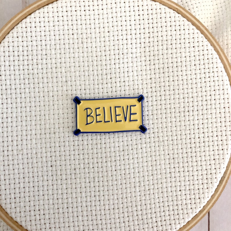 K&ouml;nnte beinhalten: Ein gelbes Banner mit blauem Rand und dem Wort "BELIEVE" in Schwarz.
