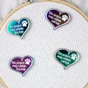 May include: Four iridescent heart-shaped pins with paw prints. Each pin has a white inscription that reads "This project may contain [dog/cat] hair".