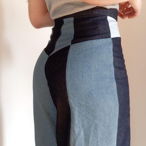 May include: A denim skirt with a patchwork design. The skirt features panels of light blue and dark blue denim, creating a geometric pattern. The waistline has a white panel. The skirt is worn with a gray top.