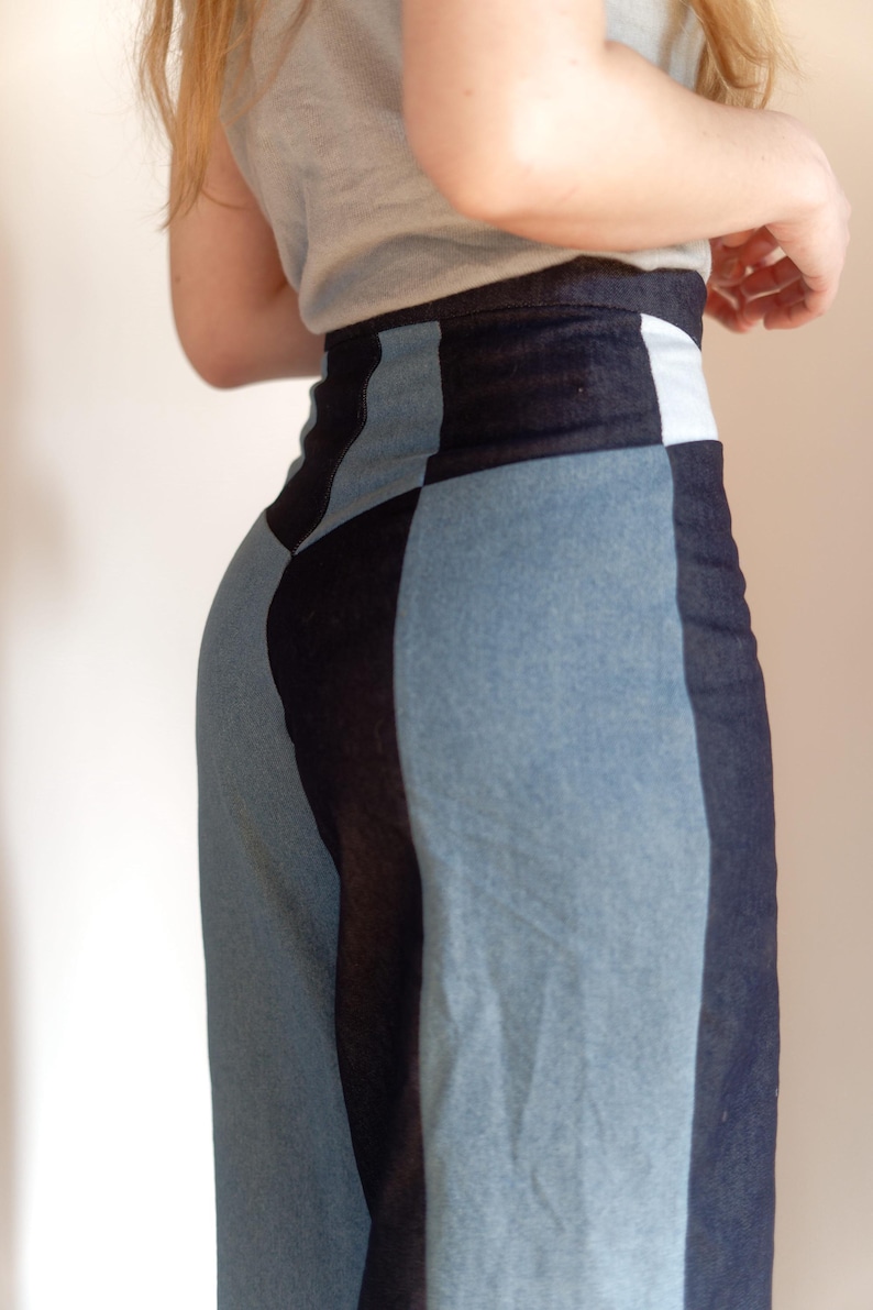May include: A denim skirt with a patchwork design. The skirt features panels of light blue and dark blue denim, creating a geometric pattern. The waistline has a white panel. The skirt is worn with a gray top.