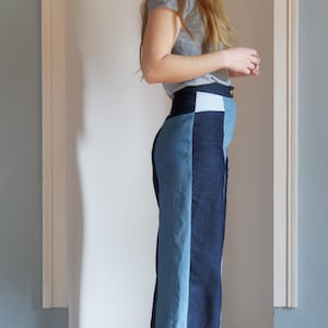 May include: High-waisted, wide-leg denim pants in a color-block design. The pants feature panels of light and dark blue denim, creating a vertical stripe effect. The waistband is a darker blue with a light blue square detail.