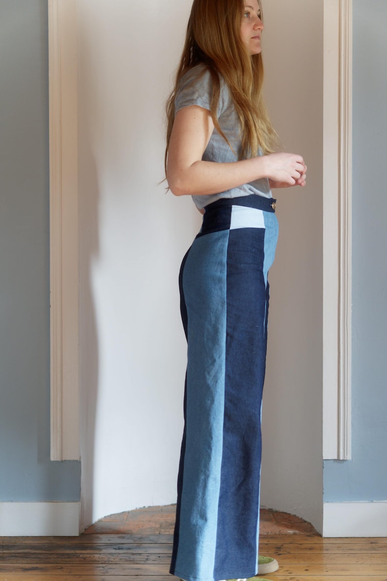 May include: High-waisted, wide-leg denim pants in a color-block design. The pants feature panels of light and dark blue denim, creating a vertical stripe effect. The waistband is a darker blue with a light blue square detail.