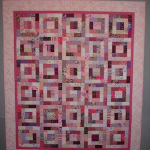 May include: A pink and purple patchwork quilt with a square pattern. The quilt is made of many different fabrics, all in shades of pink and purple.