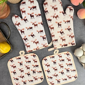 May include: Set of three kitchen oven mitts and pot holders with a brown moose pattern on a beige background. The mitts have a hanging loop and the pot holders have a square shape.