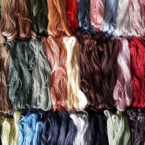 May include: A collection of colorful embroidery floss spools arranged in rows. The floss is a variety of shades of blue, green, brown, red, yellow, and white.