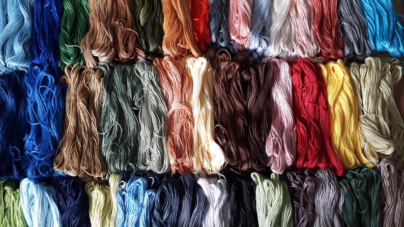 May include: A collection of colorful embroidery floss spools arranged in rows. The floss is a variety of shades of blue, green, brown, red, yellow, and white.
