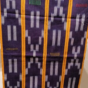 K&ouml;nnte beinhalten: Ein gewebtes Textil mit dunkelviolettem Hintergrund und einem sich wiederholenden Muster aus wei&szlig;en vertikalen Linien und geometrischen Formen. Das Design wird durch orangefarbene vertikale Streifen und kleine farbige Striche akzentuiert.