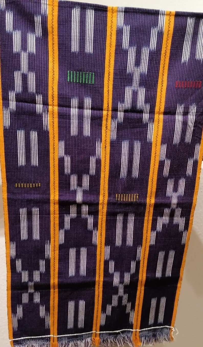 K&ouml;nnte beinhalten: Ein gewebtes Textil mit dunkelviolettem Hintergrund und einem sich wiederholenden Muster aus wei&szlig;en vertikalen Linien und geometrischen Formen. Das Design wird durch orangefarbene vertikale Streifen und kleine farbige Striche akzentuiert.
