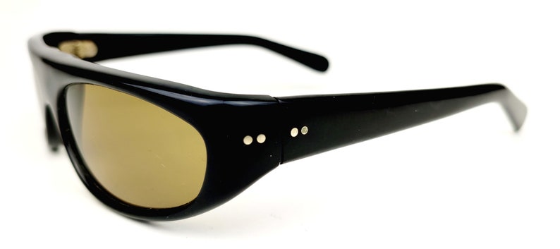 May include: Black plastic sunglasses with brown lenses. The sunglasses have a rounded shape and a thin frame.