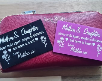 May include: Two engraved metal cards with a pink and black background. The cards have the text "Mother & Daughter" and the message "Never truly apart, maybe in distance, but never in heart." with a heart symbol and the name Matilda.
