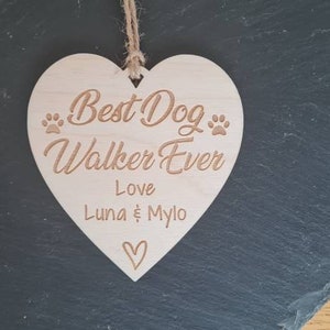 Puede incluir: Un letrero de madera en forma de coraz&oacute;n con el texto "Best Dog Walker Ever" y "Love Luna & Mylo". El letrero tiene dos huellas de patas a cada lado del texto.