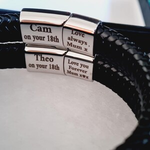 May include: Black braided leather bracelet with silver clasps. The clasps are engraved with the names "Cam" and "Theo" along with the text "on your 18th". Additional text includes "Love always, Mum x" and "Love you Forever Mum x".