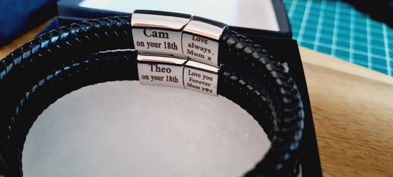 May include: Black braided leather bracelet with silver clasps. The clasps are engraved with the names "Cam" and "Theo" along with the text "on your 18th". Additional text includes "Love always, Mum x" and "Love you Forever Mum x".
