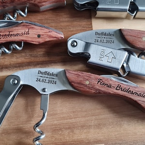 Può includere: Quattro apribottiglie con manico in legno e testo inciso. Ogni apribottiglie ha un corpo in metallo argentato con un cavatappi e un apribottiglie. Il testo sugli apribottiglie recita "Duffdales 24.02.2024", "Emma-Bridesmaid", "Aoife-Maid of Honour" e "Fiona-Bridesmaid".
