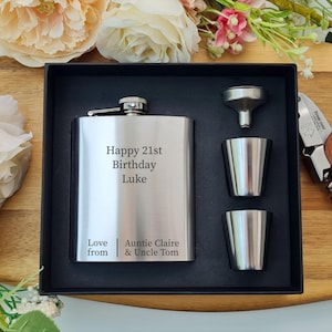 May include: A silver hip flask gift set with a black presentation box, two shot glasses, and a funnel. The flask is engraved with "Happy 21st Birthday Luke" and a message from family. A wooden-handled corkscrew is also included.
