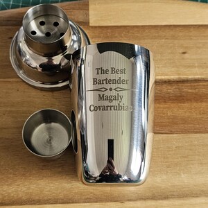 Op de afbeelding: Een zilveren cocktailshaker met een gegraveerde inscriptie die "The Best Bartender Magaly Covarrubias" luidt.