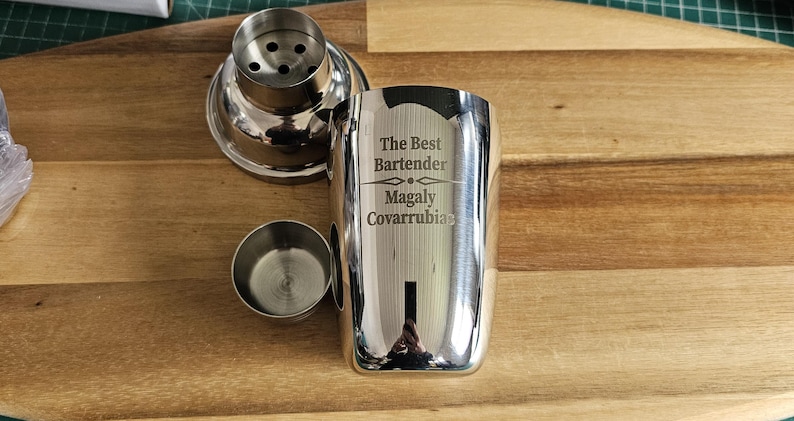 Op de afbeelding: Een zilveren cocktailshaker met een gegraveerde inscriptie die "The Best Bartender Magaly Covarrubias" luidt.