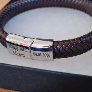 May include: A brown braided leather bracelet with a silver clasp, presented in a black gift box. The clasp is engraved with "Happy 18th Mason" and the date "04.01.2006". The bracelet is approximately 8 inches in circumference.