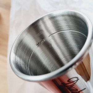 Op de afbeelding: Een maatbeker van roestvrij staal met een capaciteit van 35 ml. De beker is glanzend en heeft een geborstelde afwerking.