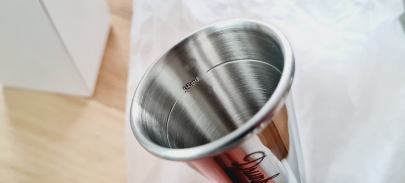 Op de afbeelding: Een maatbeker van roestvrij staal met een capaciteit van 35 ml. De beker is glanzend en heeft een geborstelde afwerking.
