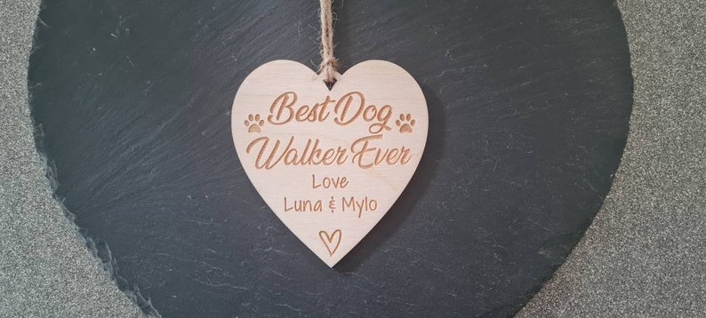 Puede incluir: Un letrero de madera en forma de coraz&oacute;n con el texto "Best Dog Walker Ever" y "Love Luna & Mylo" con huellas de patas y un peque&ntilde;o coraz&oacute;n.