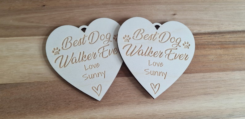 Puede incluir: Dos adornos de madera blanca en forma de coraz&oacute;n con el texto "Best Dog Walker Ever" y "Love Sunny" en cada uno.