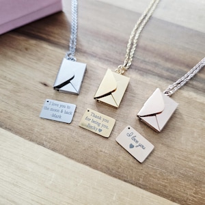 May include: Three envelope-shaped pendant necklaces in silver, gold, and rose gold, each with a matching engraved tag. The tags read "I love you to the moon & back -Mark", "Thank you for being you. Becky", and "I love you."