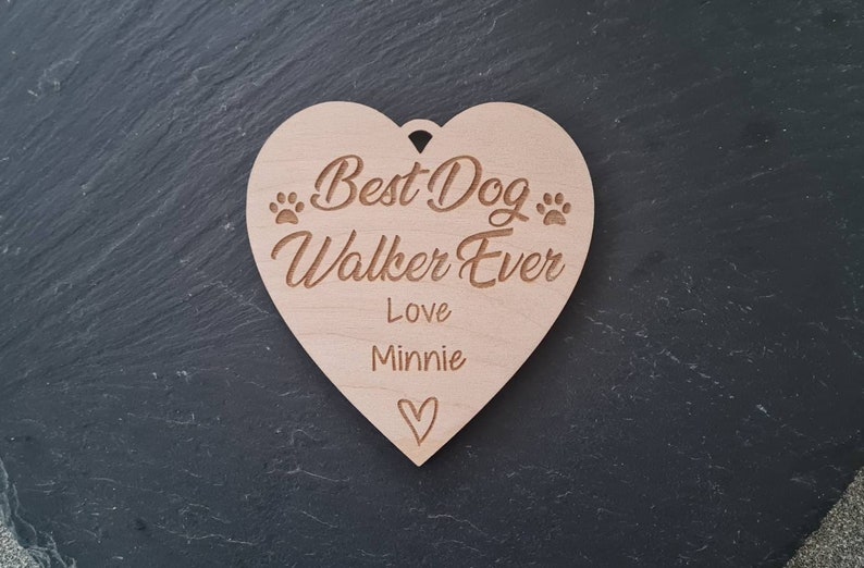 Puede incluir: Una placa de madera en forma de coraz&oacute;n con el texto "Best Dog Walker Ever" y "Love Minnie" con un peque&ntilde;o s&iacute;mbolo de coraz&oacute;n.
