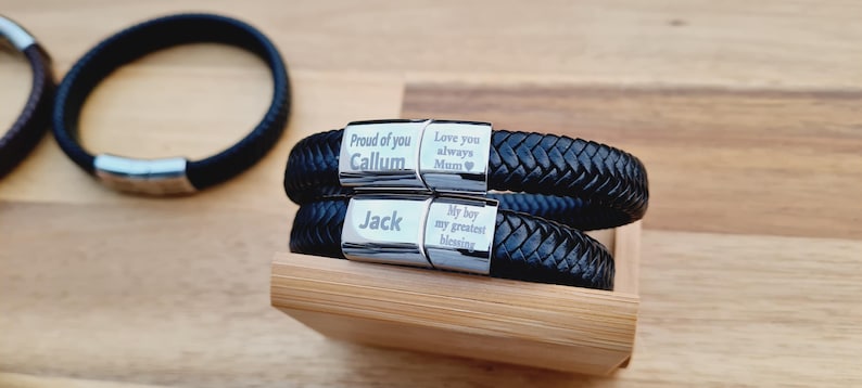 May include: Black braided leather bracelets with silver clasps. One bracelet is engraved with "Proud of you Callum" and "Love you always Mum". The other is engraved with "Jack" and "My boy my greatest blessing".